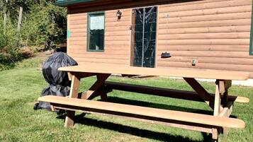 Una cabaña de madera con mesa de picnic, una parrilla y una puerta con ventana.