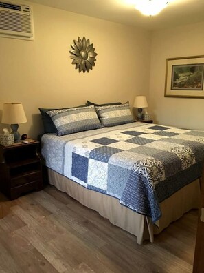 A bedroom with a bed, two bedside tables, a wall decoration, and a framed picture. - Serene Country Cabins 3 in Hyde Park, VT (Hyde Park)