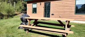 Una cabaña de madera con mesa de picnic, una parrilla y una puerta con ventana.
