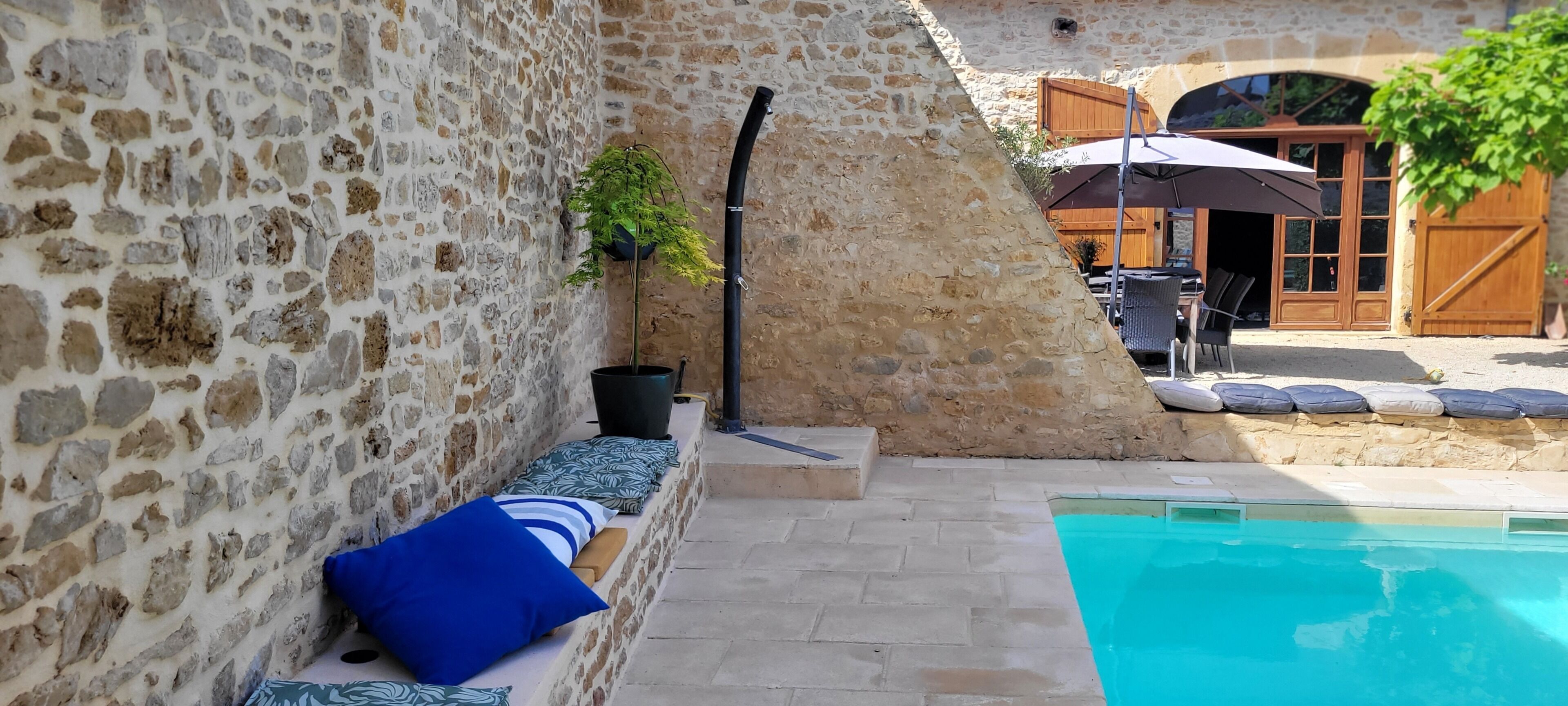 Un espace extérieur entouré de murs en pierre, avec une piscine, des sièges et une porte en bois.