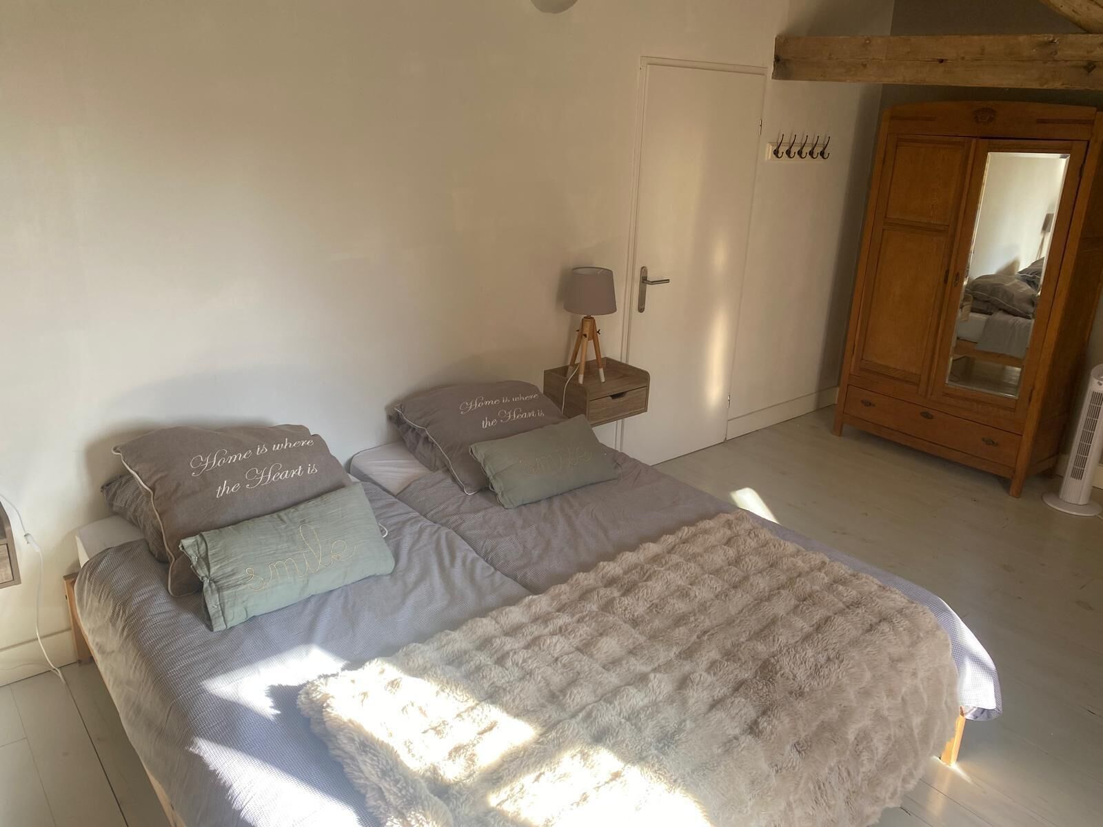 Ein Schlafzimmer mit einem Bett, Kissen, einem Nachttisch, einer Lampe, einem Kleiderschrank und einem Spiegel.