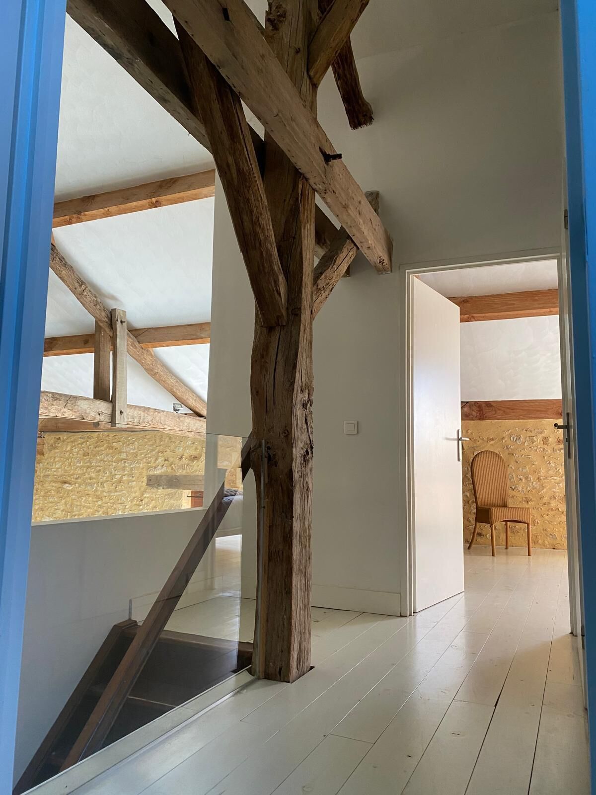 A modern interior with exposed wooden beams, a staircase, and a view of an outdoor area.