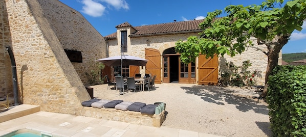 Un edificio de piedra con un patio, mobiliario exterior y una piscina.