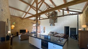 A spacious kitchen with a large island, wooden beams, stone walls, and a dining area with a table and chairs. - La Grange du Sotoul - Large house for 10 people with all comforts and private swimming pool (Soturac)