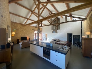 Una cocina amplia con una isla grande, vigas de madera, paredes de piedra y una zona de comedor con mesa y sillas.