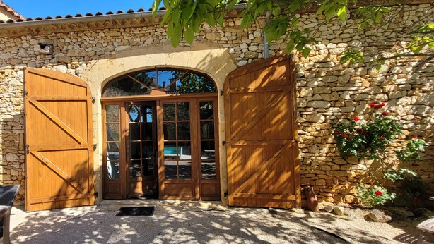 A stone building with wooden doors and a patio area. - La Grange du Sotoul - Large house for 10 people with all comforts and private swimming pool (Soturac)