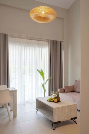 Ein modernes Wohnzimmer mit einem hellen Sofa, einem Couchtisch mit Früchten, einer Pendelleuchte und transparenten Vorhängen.