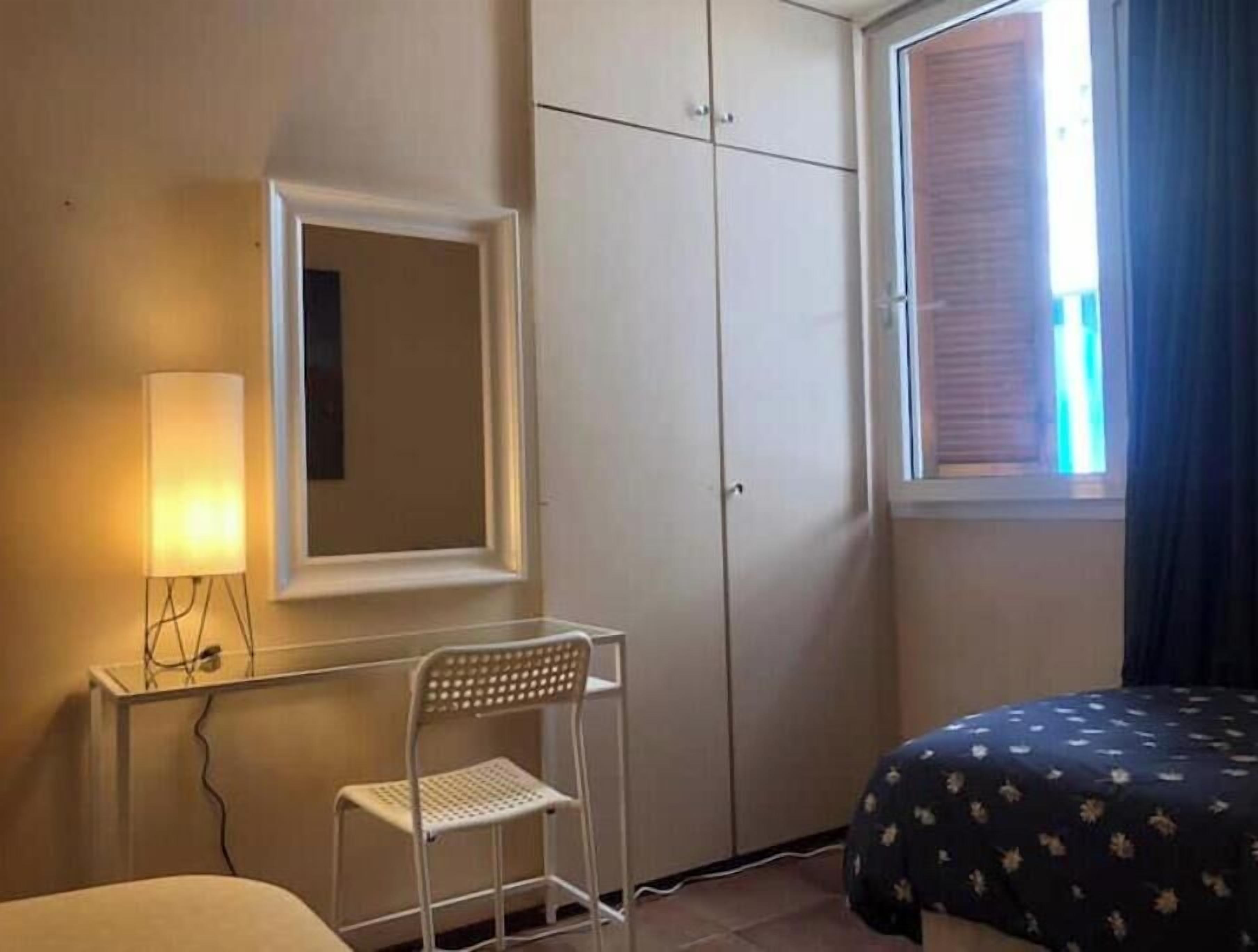 A bedroom with a bed, a desk, a chair, a wardrobe, and a window with curtains.