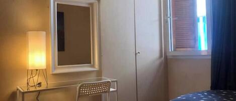 A bedroom with a bed, a desk, a chair, a wardrobe, and a window with curtains.