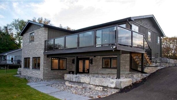 A modern two-story house with a stone facade, large windows, and a covered patio area. - Spacious Lakefront Cottage with Private Boat Launch on Chemong Lake, Near Peterborough, Ontario (Harcourt)