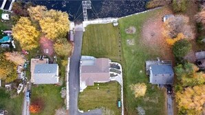 An aerial view of a residential area with three houses, a road, and a body of water. - Spacious Lakefront Cottage with Private Boat Launch on Chemong Lake, Near Peterborough, Ontario (Harcourt)