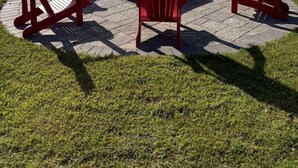 A circular outdoor seating area with red Adirondack chairs around a fire pit, overlooking a lake. - Spacious Lakefront Cottage with Private Boat Launch on Chemong Lake, Near Peterborough, Ontario (Harcourt)