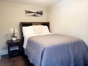 Un dormitorio con cama, un mesita de noche con un florero y un cuadro en la pared.