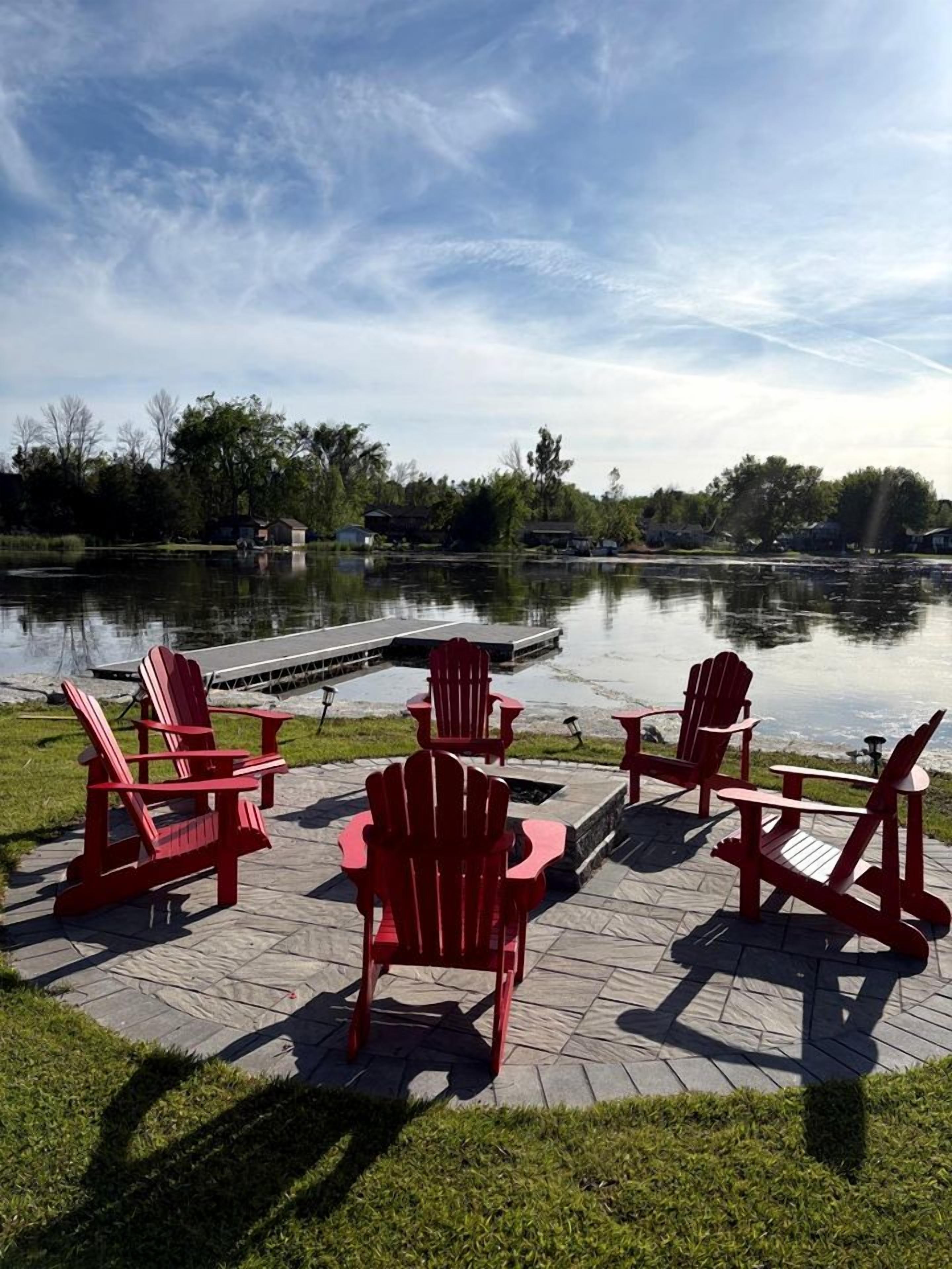 Um alpendre à beira do lago com cadeiras Adirondack e um píer.