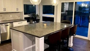 A kitchen with a central island, bar stools, pendant lighting, and a view to the outside. - Spacious Lakefront Cottage with Private Boat Launch on Chemong Lake, Near Peterborough, Ontario (Harcourt)