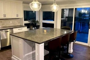 A kitchen with a central island, bar stools, pendant lighting, and a view to the outside. - Spacious Lakefront Cottage with Private Boat Launch on Chemong Lake, Near Peterborough, Ontario (Harcourt)