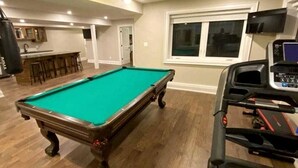A pool table in a room with a treadmill, a bar area, and a window with blinds. - Spacious Lakefront Cottage with Private Boat Launch on Chemong Lake, Near Peterborough, Ontario (Harcourt)