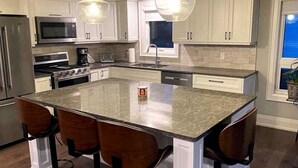 A kitchen with a large island, bar stools, stainless steel appliances, and pendant lighting. - Spacious Lakefront Cottage with Private Boat Launch on Chemong Lake, Near Peterborough, Ontario (Harcourt)