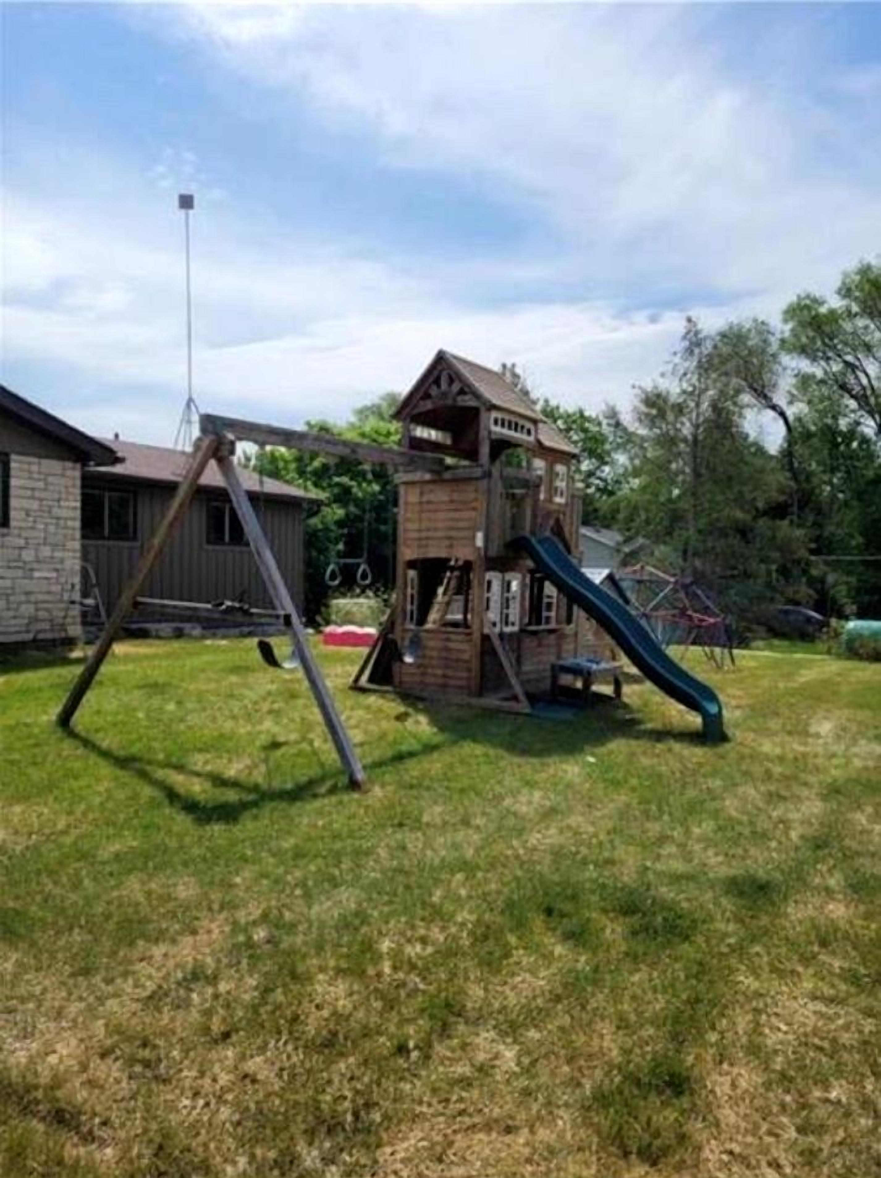 A playground with a slide and swings, a wooden playhouse, and a building with a chimney.
