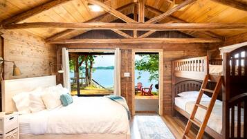 Una cabaña con interior de madera, una cama individual, una litera y vista al lago.