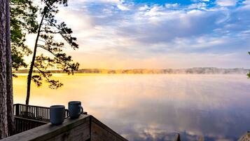 A wooden deck with a view of a calm lake and trees.
