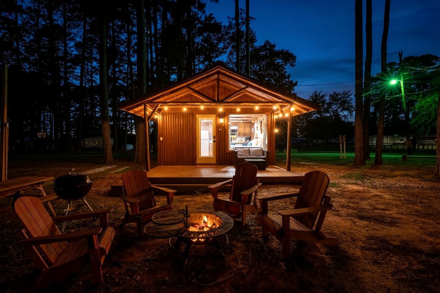 Una cabaña de madera con terraza, mobiliario exterior, una parrilla y un hogar.