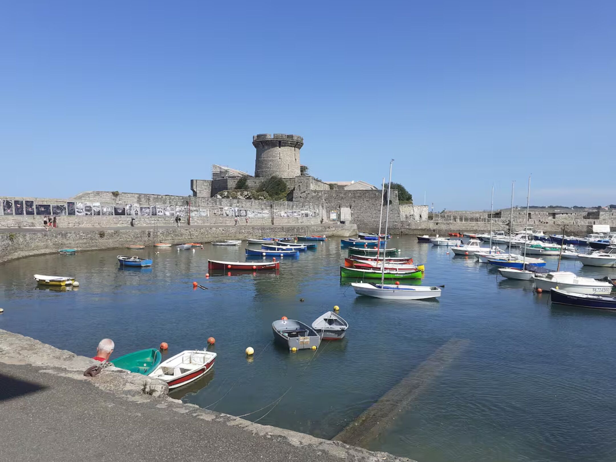 Un port avec des bateaux, un mur de pierre et une tour.