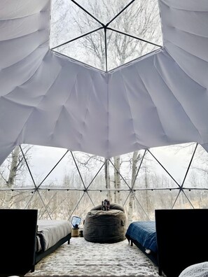 An igloo-style tent with a geometric ceiling design, a bed, a bean bag, and a small table with a lamp.