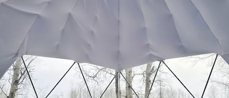 Une tente de style igloo dotée d’un plafond au design géométrique, d’un lit, d’un fauteuil poire et d’une petite table avec une lampe.