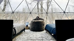 An igloo-style tent with a geometric ceiling design, a bed, a bean bag, and a small table with a lamp.