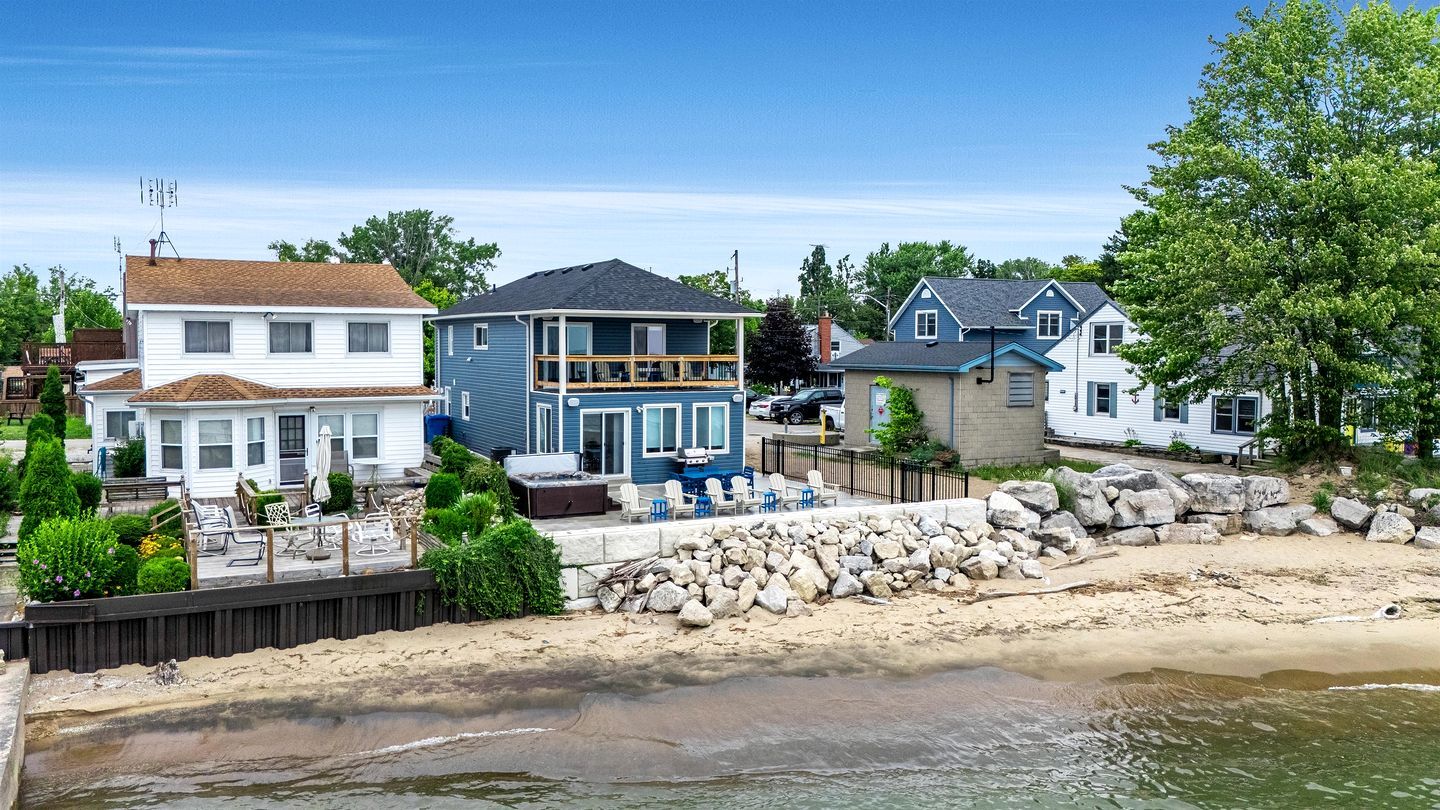 Ein Strandgrundstück mit einem großen Haus, einem kleineren Haus und einem Strandabschnitt mit Felsen und einer Holzterrasse.