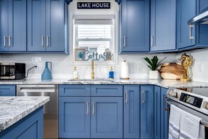 A kitchen with blue cabinets, a Bosch dishwasher, a microwave, a sink with gold handles, and a sign that reads 'LAKE HOUSE'. - Luxurious Beachfront Rental with Hot-Tub and Yard in Canada (Kingsville)