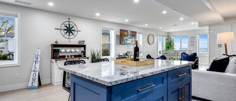 A modern kitchen with a large island, a clock on the wall, and a welcome sign.