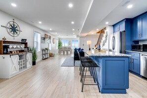 A modern kitchen with blue cabinets, a central island, and a dining area with a view. - Luxurious Beachfront Rental with Hot-Tub and Yard in Canada (Kingsville)