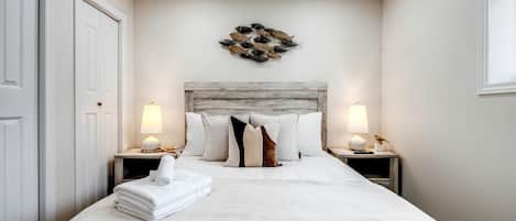 A neatly made bed with a headboard, two bedside tables with lamps, and a wall decoration above the bed.