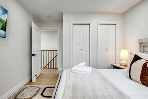 A hotel room with a bed, a nightstand with a lamp, a door, a staircase, and a painting on the wall. - Luxurious Beachfront Rental with Hot-Tub and Yard in Canada (Kingsville)