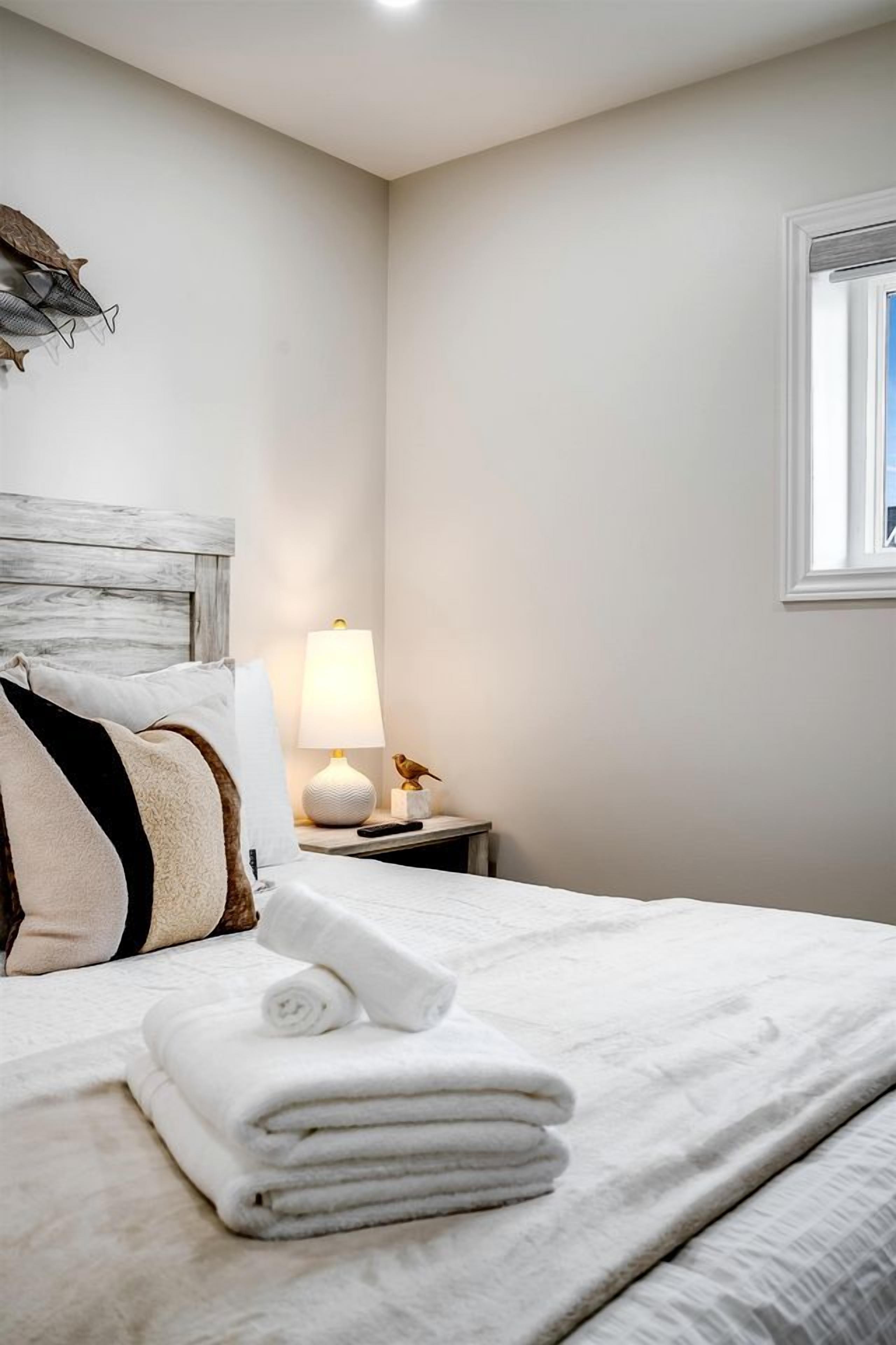 A neatly made bed with white linens, a lamp on the nightstand, and a wall-mounted shelf with decorative items.