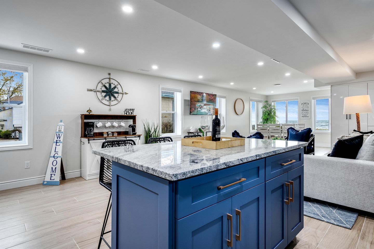 A modern kitchen with a large island, a clock on the wall, and a welcome sign.