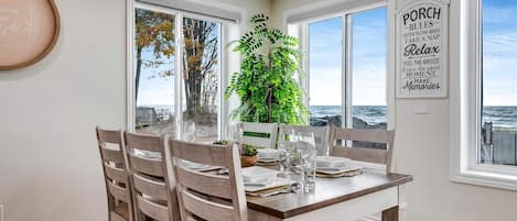 Un comedor con vista al océano, una planta grande en maceta y una pared con un letrero que dice 'Porch Rules'.
