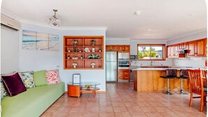 Eine moderne Küche mit Holzausstattung, ein Essbereich mit Barhocker und ein grünes Sofa mit gemusterten Kissen.