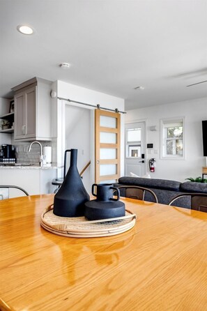 A modern kitchen with white cabinets, a wooden dining table, and a black vase. - Beachfront Cottage with Stunning Sights in Leamington, Ontario (Leamington)