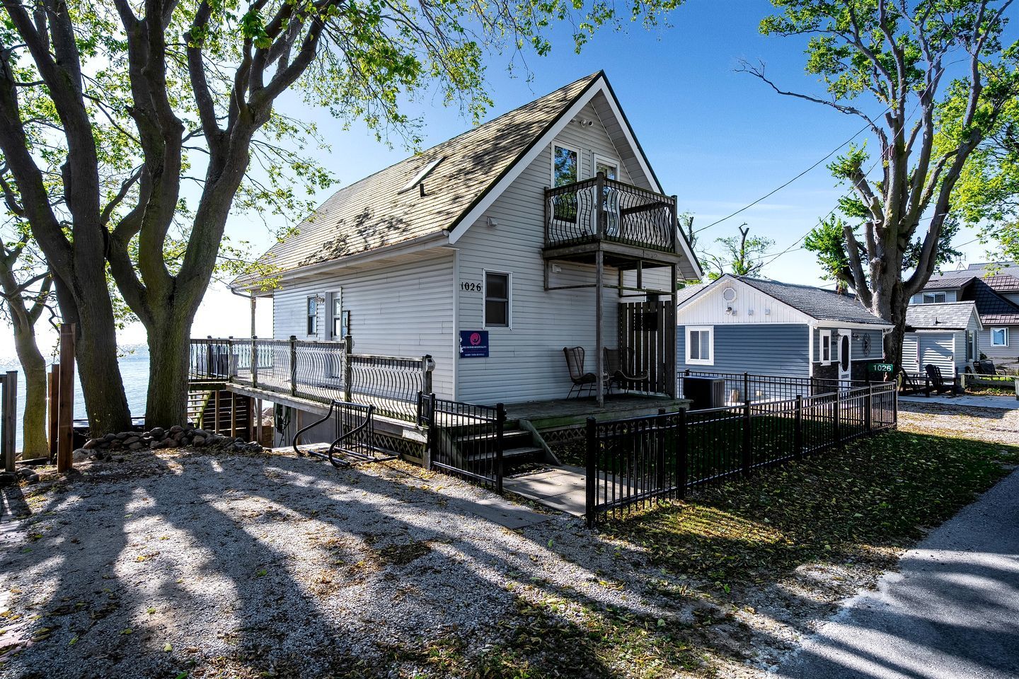 A white house with a balcony, a gravel driveway, and a wooden deck.