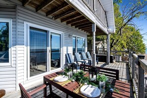A covered outdoor deck with a dining table set for two, a seating area with chairs, and a view of the ocean. - Beachfront Cottage with Stunning Sights in Leamington, Ontario (Leamington)