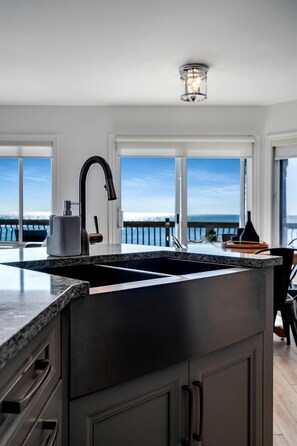 Une cuisine moderne dotée d’un grand îlot central, d’un robinet noir et offrant une vue sur l’océan grâce à de grandes fenêtres.