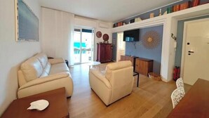 A living room with a sofa, armchairs, a coffee table, and a TV. - Hostdomus - Myros Apartment (Finale Ligure)