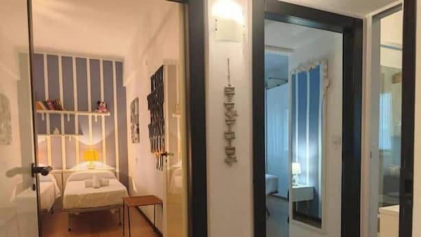 A narrow hallway leading to a bedroom with a bed, bedside table, and a small table. - Hostdomus - Myros Apartment (Finale Ligure)