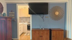A room with a wooden cabinet, a television mounted on the wall, and a decorative wall piece. - Hostdomus - Myros Apartment (Finale Ligure)