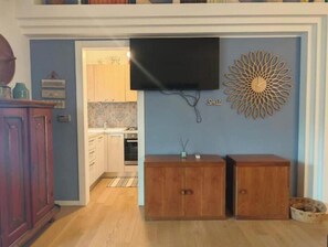 Ein Zimmer mit einem Holzschrank, einem an der Wand montierten Fernseher und einem dekorativen Wandbild.