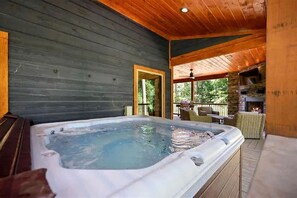A hot tub in a wooden cabin with a patio area and a fireplace. - Surrounded by Tall Pines Forest Views with Hot Tub, Game Room & Outdoor Fireplace in Broken Bow, Oklahoma (Broken Bow)