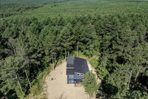 A single-story house with a dark roof, surrounded by dense forest. - Surrounded by Tall Pines Forest Views with Hot Tub, Game Room & Outdoor Fireplace in Broken Bow, Oklahoma (Broken Bow)